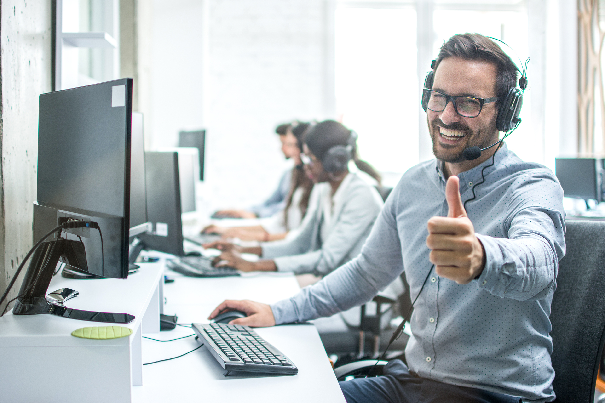 Image of man giving the thumbs up while sitting at a desk with headphones on