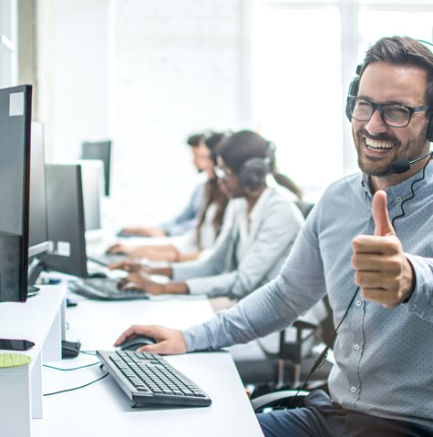 Image of man giving the thumbs up while sitting at a desk with headphones on