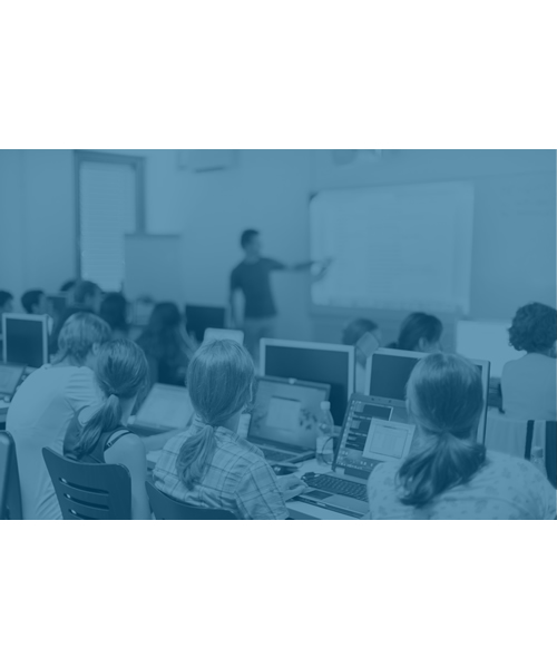 A man standing in front of a white board pointing to information as he teaches students sitting at their computers