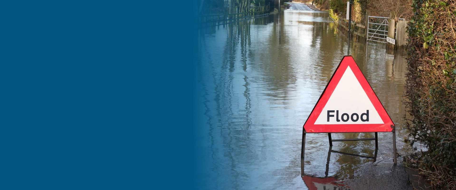 An image of a flood sign in the street with flooding around it